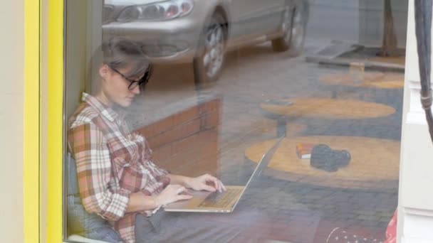 Young woman in glasses work with laptop in the coffee shop - Materiał filmowy, wideo