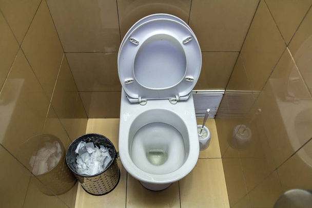 Interieur van eenvoudige toilet-toilet, bekijken van bovenaf. Witte keramische WC toilet-keramische bril op kopie ruimte achtergrond van licht beige tegel wanden en basis. Ontwerp en hygiëne concept. - Foto, afbeelding