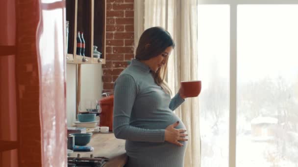 Adult pregnant woman strokes the belly and holds a red cup - Metraje, vídeo