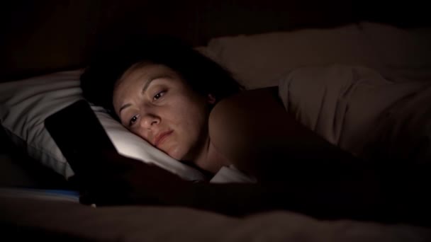 Νεαρή γυναίκα στο κρεβάτι με smartphone. Γυναίκα με πρωταγωνιστή σε συσκευή κινητό τηλέφωνο πριν πάτε για ύπνο σε ανάλυση 4k - Πλάνα, βίντεο