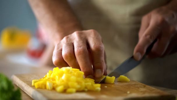 Mature husband cooking vegetable salad, cutting yellow pepper, culinary show - Foto, Imagem
