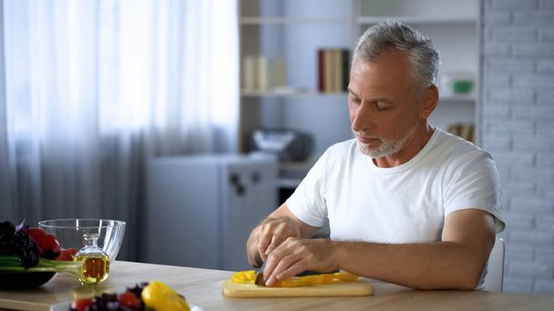 Disabled husband cooking dinner in kitchen, cutting vegetables for healthy meal - Fotó, kép