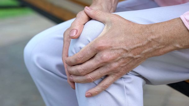Old lady touching knee, sitting on bench, pain in joints, problems with knees - Fotó, kép