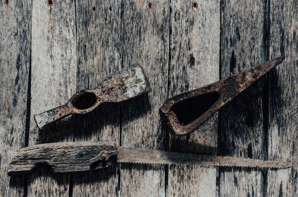 Old rusted hammer, cleaver and hacksaw with wooden handle on wooden background. - 写真・画像