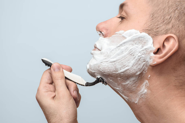 Crop shot of a man shaving with a razor on a grey background. Side view. Photo with copy space. - Zdjęcie, obraz
