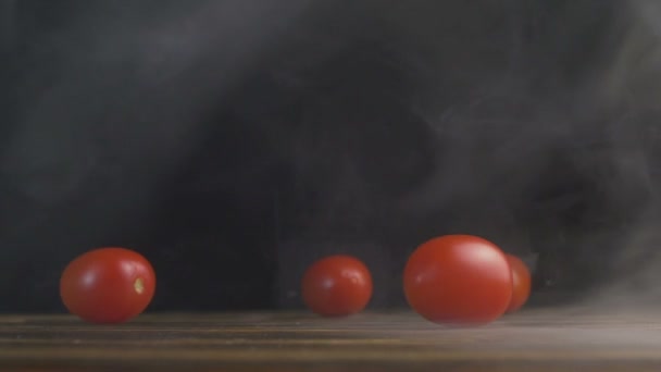 Red small tomatoes or Cherry tomato roll across the table in the smoke in slowmo - Imágenes, Vídeo