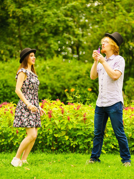 Happy funny hipster couple playing together blowing soap bubbles outdoor in spring park. - Φωτογραφία, εικόνα