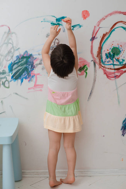 A little girl, 3 years old, painted an arched look with paint and a brush on the wall of her room. - Fotografie, Obrázek