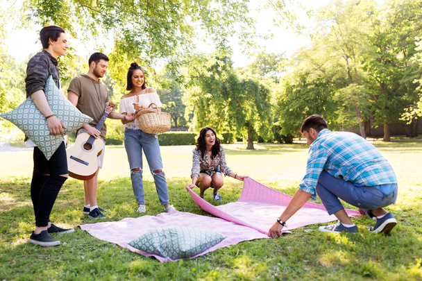 friends arranging place for picnic at summer park - Photo, Image