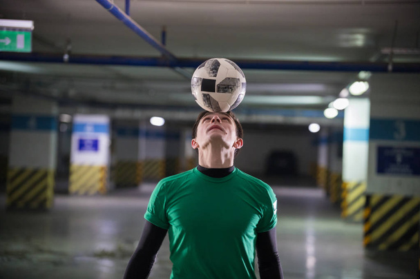 Jalkapalloidea. Jalkapalloilija pitää palloa päässään. Pysäköintialue
 - Valokuva, kuva