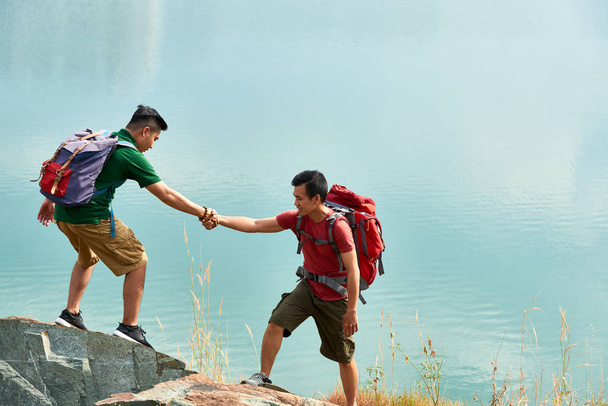 Jóvenes excursionistas ayudándose unos a otros al subir la montaña
 - Foto, imagen