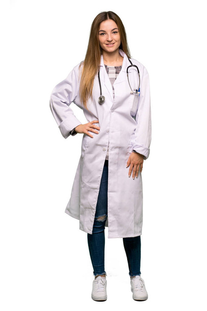 Volledige lichaam jonge dokter vrouw poseren met de armen op heup- en glimlachend op geïsoleerde achtergrond - Foto, afbeelding