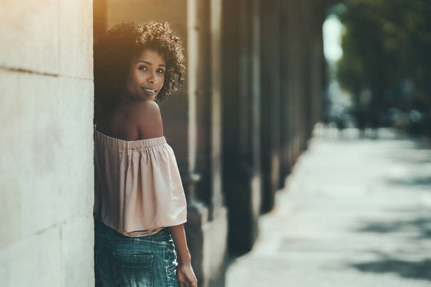 The portrait of a young cute Brazilian woman leaning against the column outdoors; a dazzling smiling African-American female near the stone pillar, with a copy space place for your advertising text - Zdjęcie, obraz