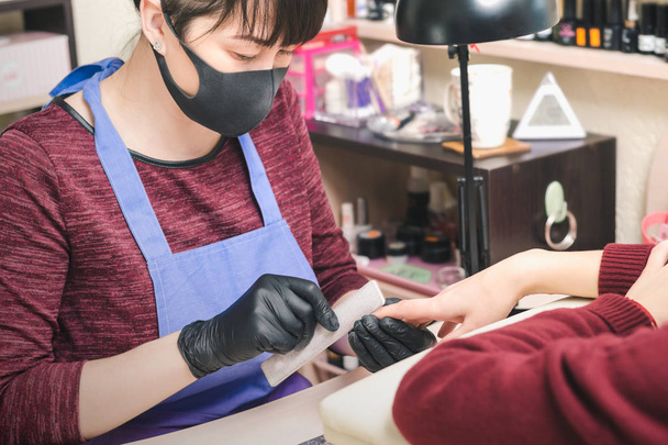 Manicurist in black latex gloves form the shape of a client's nail in a beauty salon. - Photo, Image