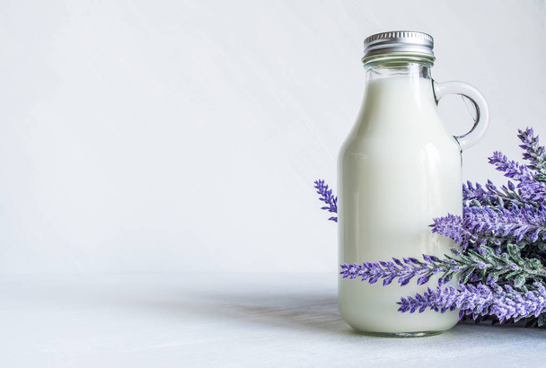 Vintage bottle with milk, near a branch of lavender flowers on a white vintage background - Foto, afbeelding