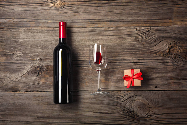 Bottle of wine with wine glass and gift box on wooden background. Top view with copy space for your text - Photo, Image