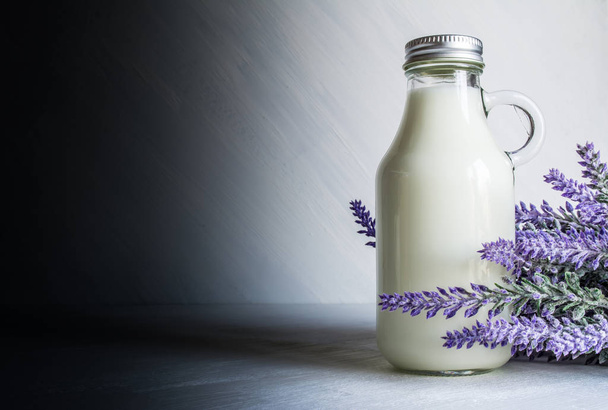 Vintage bottle with milk, near a branch of lavender flowers on a white vintage background - Valokuva, kuva