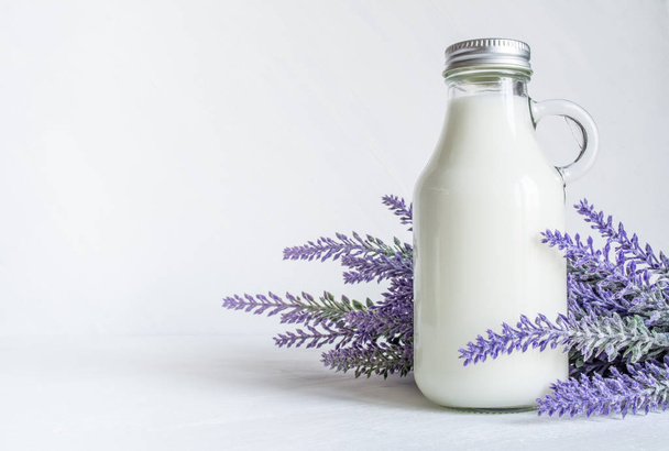 Vintage bottle with milk, near a branch of lavender flowers on a white vintage background - Photo, image