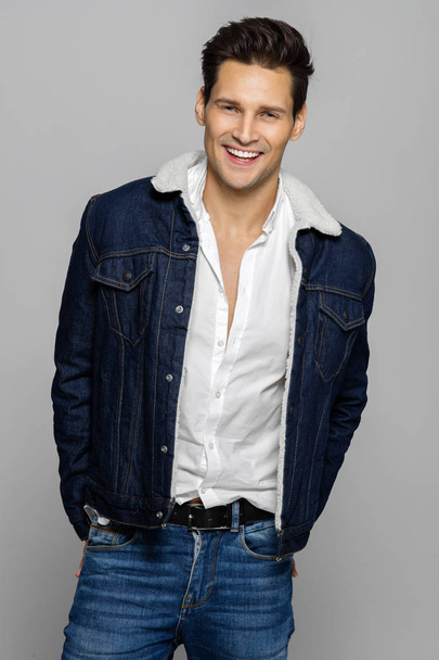 Young handsome man wearing jeans outfit and smiling isolated over gray background - Foto, Imagem