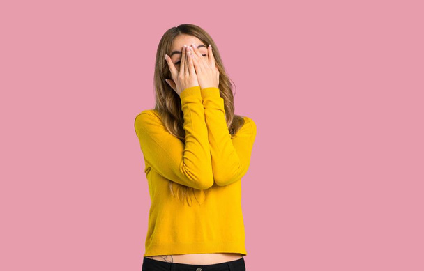 молода дівчина з жовтим светром, що закриває очі руками і дивиться через пальці на ізольованому рожевому фоні
 - Фото, зображення