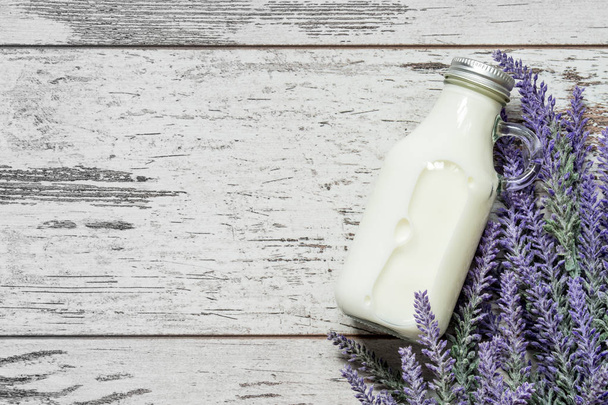 Vintage glass bottle with milk next to a branch of lavender flowers on a vintage wooden background. View from above. - Foto, Imagem