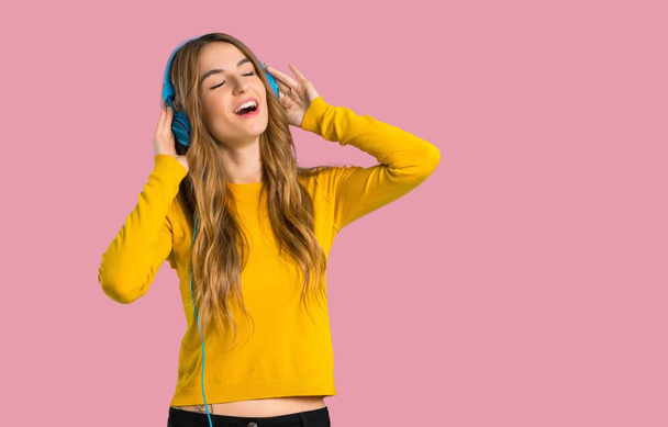 jeune fille avec pull jaune écoutant de la musique avec écouteurs sur fond rose isolé
 - Photo, image