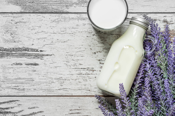 Vintage glass bottle with milk and a glass with milk next to a branch of lavender flowers on a vintage wooden background. View from above. - Photo, image