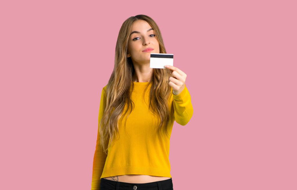 niña con suéter amarillo sosteniendo una tarjeta de crédito sobre fondo rosa aislado
 - Foto, Imagen