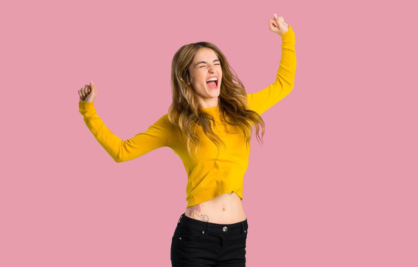 jovem com suéter amarelo feliz e pulando sobre fundo rosa isolado
 - Foto, Imagem