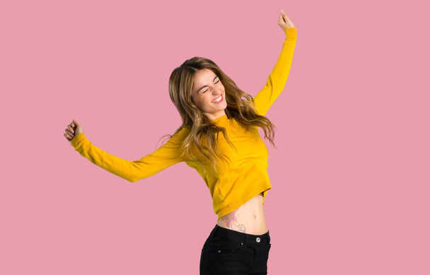 young girl with yellow sweater happy and jumping on isolated pink background - Фото, изображение