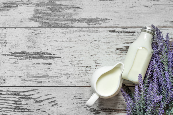 Vintage glass bottle with milk and a beautiful white jug next to a branch of lavender flowers on a vintage wooden background. View from above. - Foto, immagini