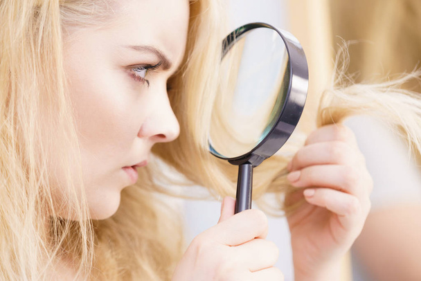 Split ends problem, dry effect, haircare concept. Unhappy blonde woman looking at destroyed damaged hair through magnifying glass - Photo, Image