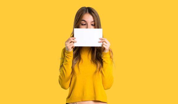 young girl with yellow sweater holding a placard for insert a concept on isolated yellow background - Photo, Image