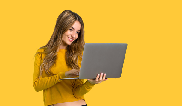 young girl with yellow sweater with laptop on isolated yellow background - Photo, Image