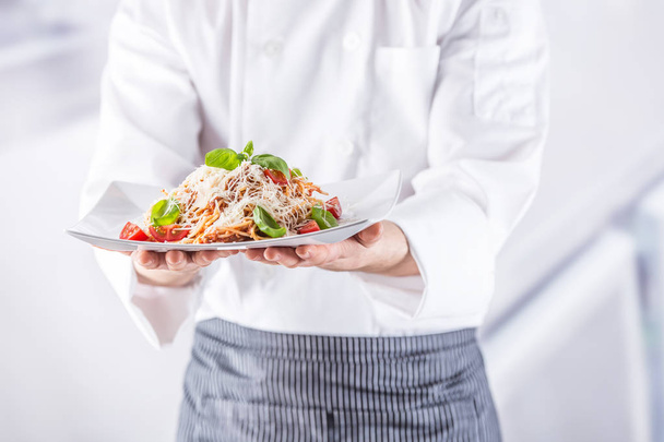 Chef in restaurant kitchen holding plate with italian meal spaghetti bolognese. - Фото, изображение