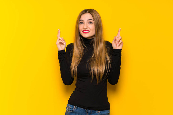 Young pretty woman over yellow background with fingers crossing and wishing the best - Фото, зображення