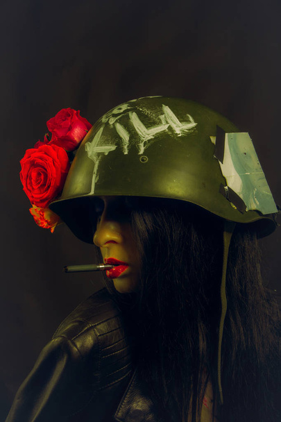 Sexy glamour girl in helmet smoking cigarette over dark background - Fotó, kép