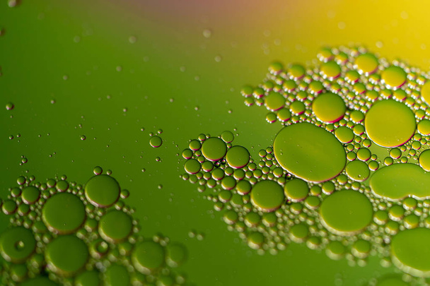 Een close-up van olie druppels op een wateroppervlak met een gekleurde achtergrond. - Foto, afbeelding