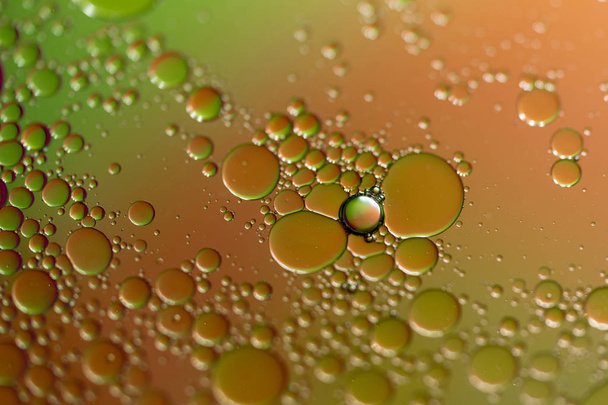 Ένα closeup του σταγονίδια του πετρελαίου στην επιφάνεια του νερού με ένα έγχρωμο φόντο. - Φωτογραφία, εικόνα