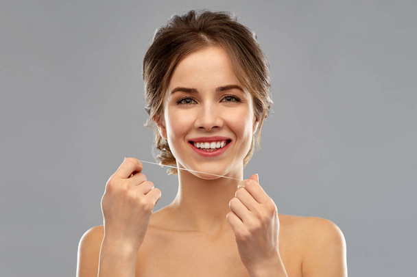 health care, hygiene and people concept - happy young woman with dental floss cleaning teeth over grey background - Valokuva, kuva