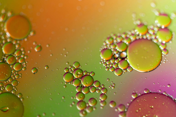 A closeup of oil droplets on a water surface with a colored background. - Фото, изображение
