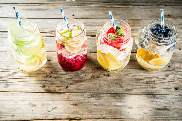 Selection various fruit and berry lemonade drinks, refreshment infused water, in mason jars, with fresh strawberry, lemon, lime, oranges, blueberry, wooden background copy space - Photo, Image