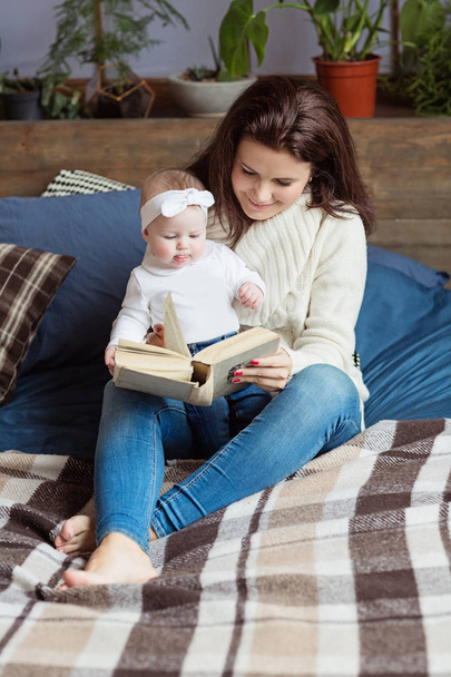 Mother and little daughter are playing, reading a book, lying and relax in the bed. Happy family concept - Фото, изображение