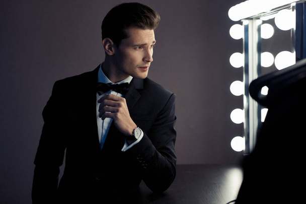 Stylish man in black suit looking at mirror with lights - Foto, Imagen