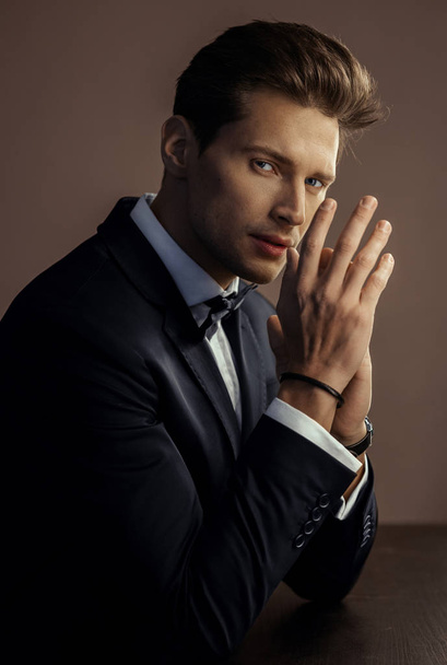 Portrait of handsome man in black suit rubbing his hands and looking at camera - Foto, afbeelding