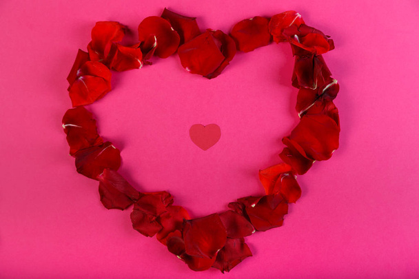Heart of rose petals on a pink background with a red cardboard heart inside. - Photo, Image