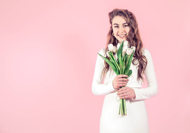 Chica joven con tulipanes blancos en sus manos sobre un fondo de color, el concepto de día de la mujer y vacaciones
 - Foto, imagen