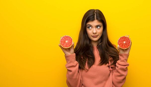 Teenager girl with pink sweatshirt on yellow background with oranges - Photo, Image