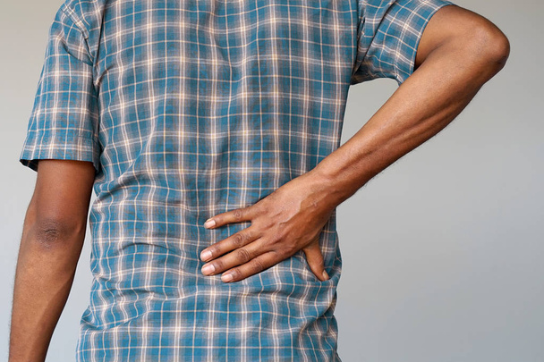 Nahaufnahme eines Afrikaners mit Nierenschmerzen, isoliert auf grauem Hintergrund. Mann mit Rückenschmerzen umklammert ihre Hand an ihren unteren Rücken. Mann leidet unter Rippenschmerzen, Bauchschmerzen. - Foto, Bild