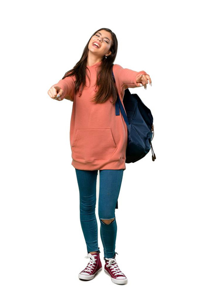 A full-length shot of a Teenager girl with sweatshirt and backpack points finger at you while smiling - Valokuva, kuva
